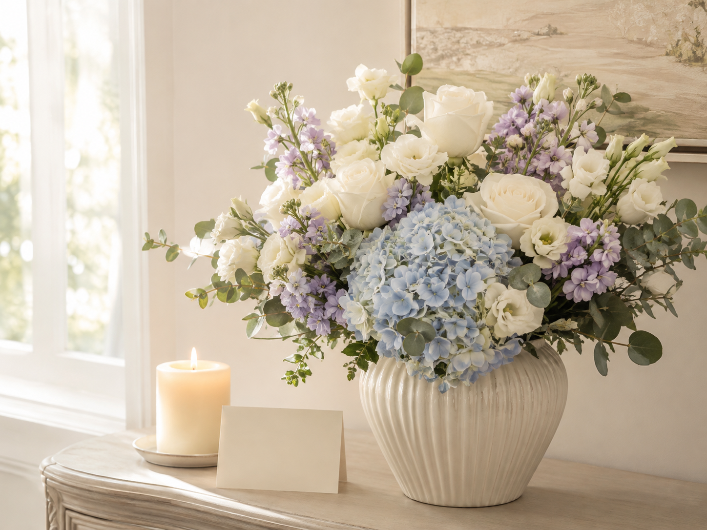 Peaceful white, lavender, and blue sympathy arrangement beside a candle